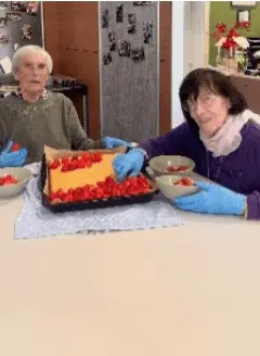 Senior und Betreuerin schneiden gemeinsam einen Kuchen an.