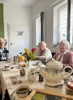 Seniorinnen und Senioren sitzen gemeinsam bei Kaffee und Kuchen an einem festlich gedeckten Tisch.