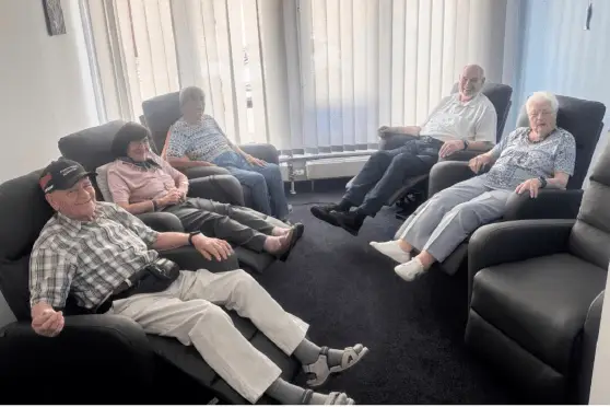 Seniorinnen und Senioren sitzen entspannt gemeinsam im Aufenthaltsraum der Tagespflege.