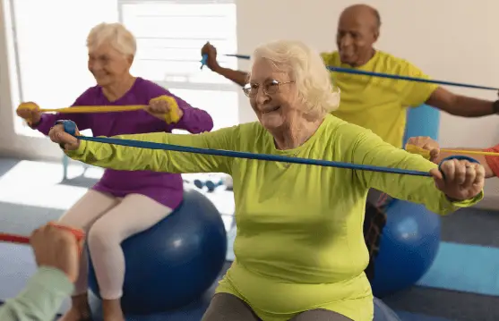 Seniorinnen nehmen mit Gymnastikbändern an einer gemeinsamen Bewegungsübung teil.